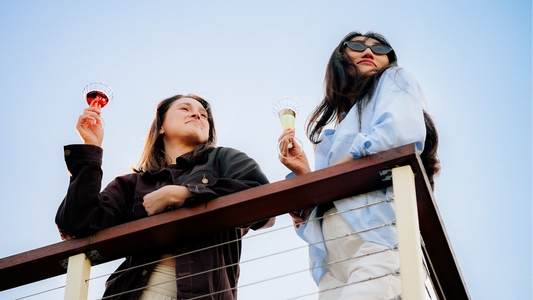 Two women standing on a balcony drinking wine out of Maebel Audrey Wine Glasses